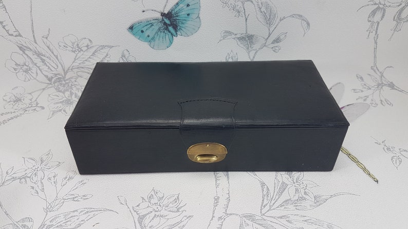 May include: A black leather jewelry box with a gold latch. The box has a textured surface and a raised design on the lid.