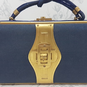 May include: A vintage blue velvet clutch with a gold metal frame and a decorative clasp. The clutch has a top handle.