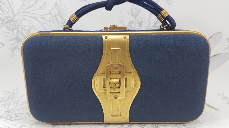 May include: A vintage blue velvet clutch with a gold metal frame and a decorative clasp. The clutch has a top handle.