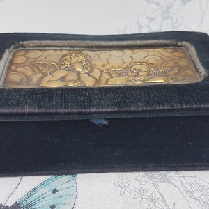 May include: A small, black velvet box with a gold-toned embossed image of two cherubs on the lid.