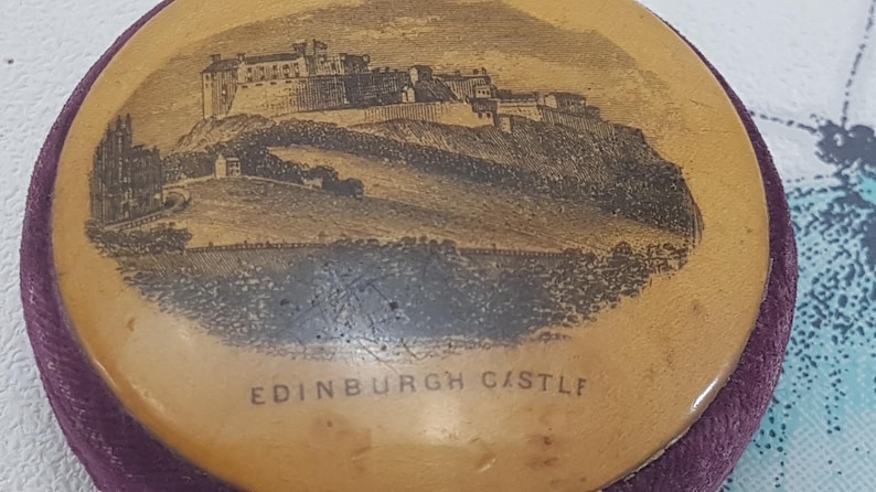 May include: A round, wooden trinket box with a purple velvet lining. The lid features a black and white image of Edinburgh Castle with the text "EDINBURGH CASTLE" printed below the image.