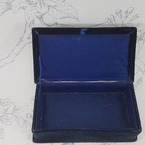 May include: A small, rectangular box with a black velvet exterior and a blue velvet interior. The box is open and empty.