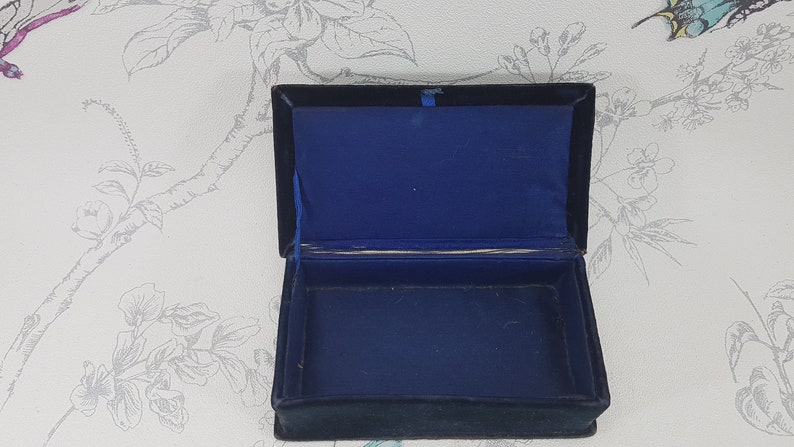 May include: A small, rectangular box with a black velvet exterior and a blue velvet interior. The box is open and empty.