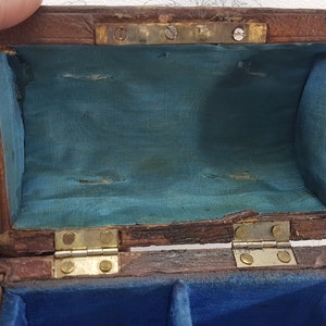 May include: A small wooden box with a hinged lid. The inside of the box is lined with blue fabric. The box has two compartments inside.
