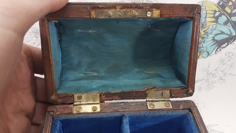 May include: A small wooden box with a hinged lid. The inside of the box is lined with blue fabric. The box has two compartments inside.