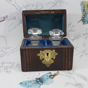 May include: A wooden box with a brass lock and key, containing two glass bottles with stoppers. The box is lined with blue velvet and has a decorative brass design on the front.