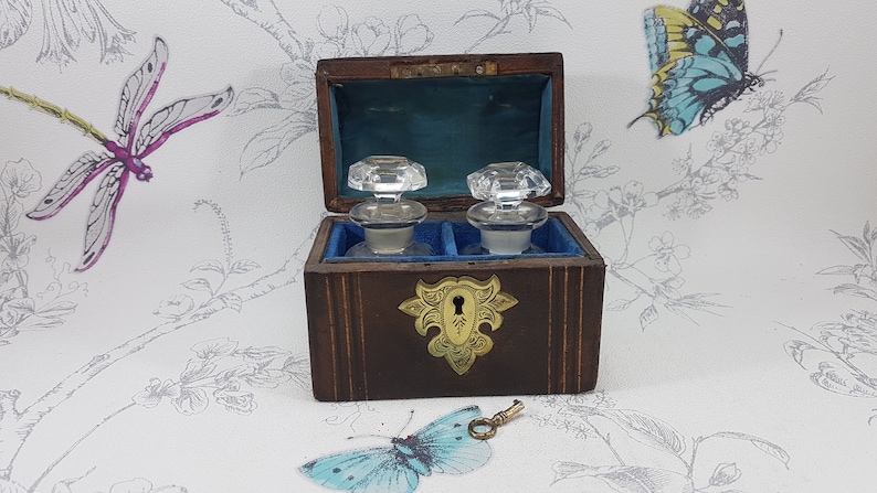 May include: A wooden box with a brass lock and key, containing two glass bottles with stoppers. The box is lined with blue velvet and has a decorative brass design on the front.