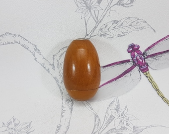 May include: A wooden egg-shaped box with a light brown finish. The box is closed and has a smooth surface.
