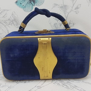 May include: A blue velvet handbag with a gold metal frame and handle. The handbag has a gold metal clasp and a decorative gold metal design on the front.