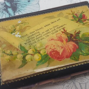 May include: A black, rectangular box with a floral design on the front. The design features a pink rose, white flowers, and green leaves. The box has a gold trim and the text "Think, dear friend, when thou art pondering Orr the past, so sad to thee, With its many scenes and changes, Think of me, Oh! think of me." and "Patent" are printed on the front.