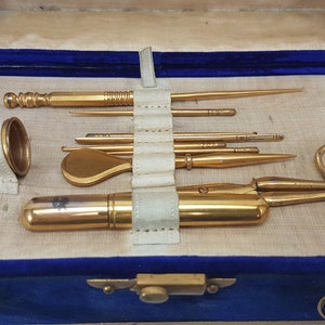 May include: A vintage sewing kit in a blue velvet case with gold-toned tools, including scissors, a thimble, and needles.