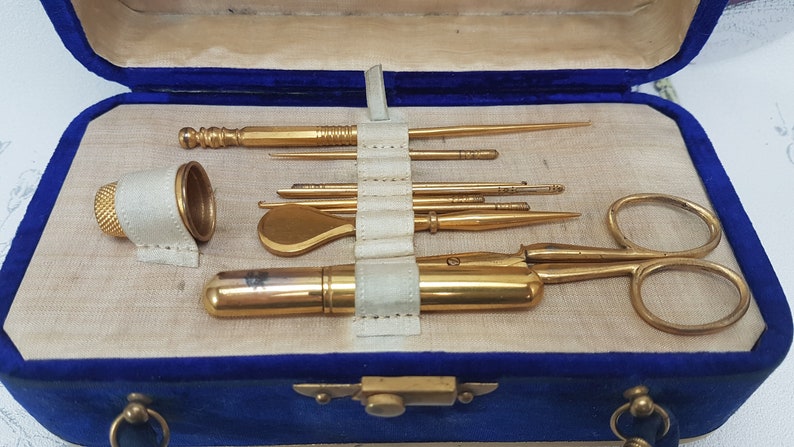 May include: A vintage sewing kit in a blue velvet case with gold-toned tools, including scissors, a thimble, and needles.