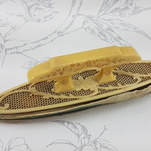 Könnte beinhalten: Ein vintage, cremefarbener, ovaler Nagelpuffer mit einem dekorativen Griff. Der Griff hat ein florales Design und ist aus dem gleichen Material wie der Puffer.