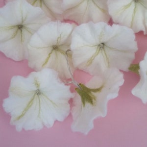 Könnte beinhalten: Eine Lichterkette aus weißen Filzblumen mit grünen Zentren. Die Lichter sind mit einem klaren Draht verbunden und eignen sich perfekt, um jedem Raum einen Hauch von Verspieltheit zu verleihen.