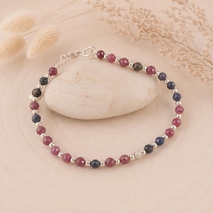 May include: A beaded bracelet featuring alternating faceted dark pink and deep blue gemstone beads interspersed with small, round, polished silver-tone metal beads. The bracelet includes a silver-tone lobster claw clasp closure.