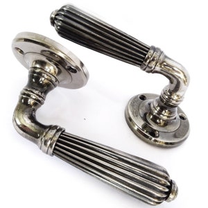 May include: A pair of antique silver door handles. The levers feature a ribbed design, and the circular bases have screw holes. The handles are curved, showcasing a vintage style.