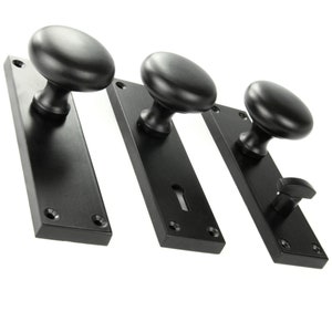 May include: Three black door knobs with square backplates. The knobs are round and have a smooth finish. The backplates have a keyhole and two screw holes.