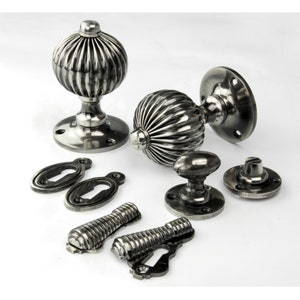 May include: A set of antique silver door knobs with a ribbed design. The set includes two knobs, two escutcheons, two keyhole covers, and two spindle covers.