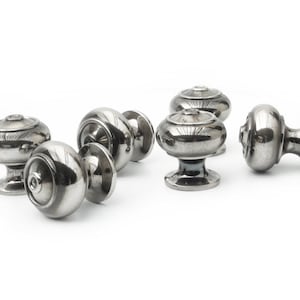 May include: A collection of silver-coloured cabinet knobs with a rounded design, arranged on a white surface. The knobs feature a decorative top and a circular base. The knobs are made of shiny metal.
