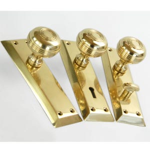 May include: Three polished brass door knobs with matching backplates. The knobs have a rounded, fluted design. The backplates are rectangular with rounded corners.