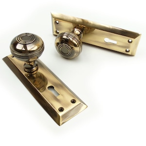 May include: Two antique brass door handle sets. Each set includes a round doorknob and a rectangular backplate with a keyhole. The brass has a warm, aged patina. The doorknobs have a grooved design.