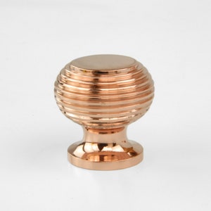 May include: A copper cabinet knob with a round, ribbed design. The knob has a smooth, polished finish.