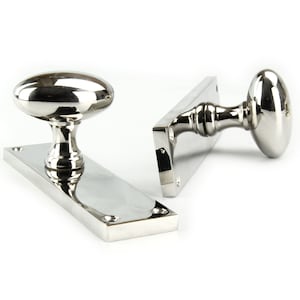 May include: A pair of polished chrome door knobs with oval-shaped handles. The knobs are mounted on rectangular plates.