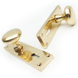 May include: Two polished brass door knobs with keyhole plates. The knobs are round and have a smooth, shiny finish. The plates are rectangular and have a keyhole in the centre.
