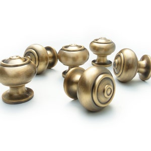 May include: Six antique brass cabinet knobs with a round, slightly domed shape and a raised ring around the edge. The knobs have a slightly textured finish.