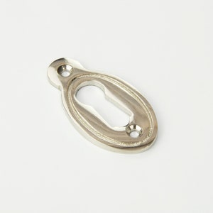 May include: A silver oval keyhole cover with a decorative border.