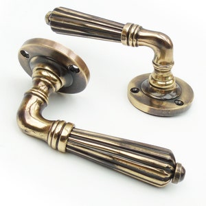 May include: A pair of antique brass door handles with a fluted design. The handles have a rounded shape and are attached to round plates.