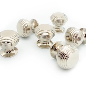 May include: Six silver cabinet knobs with a ridged design. The knobs are round and have a small base.