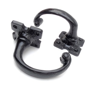 May include: Two black cast iron door handles with a square base and a curved handle. The handles are designed to be mounted on a door.