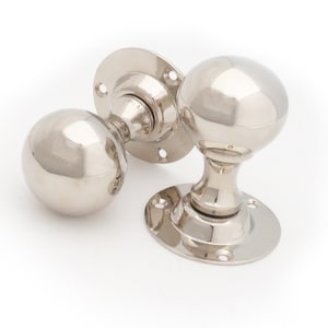 May include: Two polished nickel door knobs with round, smooth handles and circular backplates.