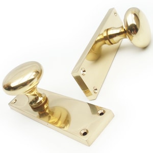 May include: Two polished brass door knobs with rectangular backplates. The knobs are oval shaped and have a smooth, shiny finish.