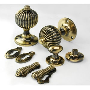 May include: Set of antique brass door knobs with a ribbed design. The set includes two door knobs, two escutcheons, two keyhole covers, and two knobs for a privacy lock.