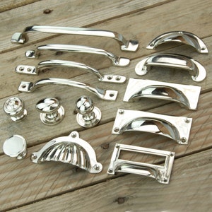 May include: A collection of polished nickel cabinet hardware, including pulls, knobs, and drawer pulls. The hardware is arranged on a wooden surface.