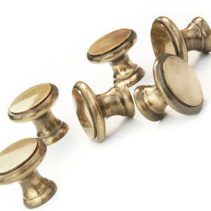 May include: Six antique brass cabinet knobs with a rounded top and a decorative ring around the top edge. The knobs are arranged in a scattered pattern on a white surface.