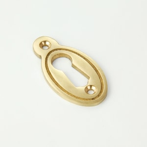 May include: A brass keyhole cover with an oval shape and a decorative border. The cover has a keyhole cut out in the centre.