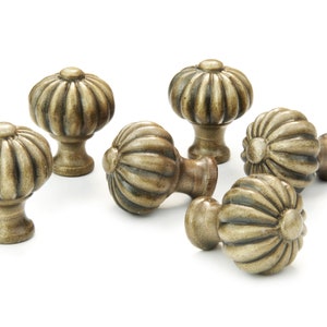 May include: A selection of antique bronze cabinet knobs, each with a pumpkin-shaped design. The knobs feature a ribbed texture and a warm, aged finish. Some are upright, others are lying down, all set against a white backdrop.