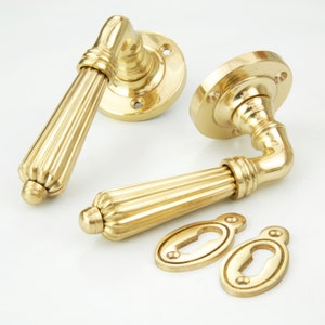 May include: Two gold door handles with a fluted design and matching keyhole covers. The handles are made of polished brass and have a traditional style.