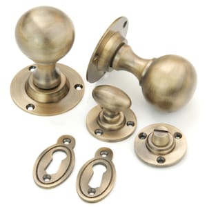 May include: A set of antique brass door knobs and escutcheons. The knobs are round and have a smooth finish. The escutcheons are oval and have a keyhole.