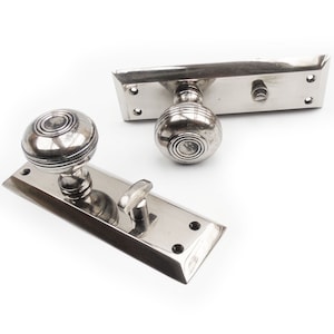 May include: A pair of polished nickel door handles with a round knob and a rectangular backplate. The handles have a simple, elegant design.