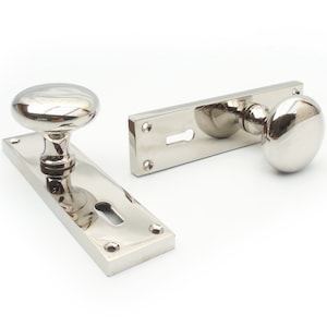 May include: A pair of polished nickel door handles with a traditional design. The handles have a round knob and a rectangular backplate with a keyhole.
