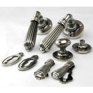May include: A set of silver door handles with a fluted design. The set includes two door handles, two escutcheons, two keyhole covers, and a knob. The handles are made of metal and have a polished finish.