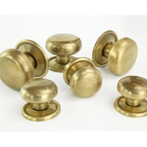 May include: A selection of antique brass door knobs. The knobs are rounded with a circular base. The brass has a warm, golden tone, and the knobs are arranged against a white backdrop.