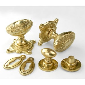 May include: Set of ornate brass door knobs and keyhole escutcheons. The knobs feature an oval shape with intricate floral designs. The escutcheons are oval with keyholes.