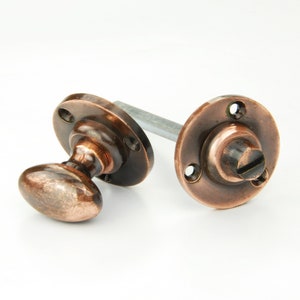 May include: A pair of antique-style door knobs with a copper finish. The knobs have a round base and a rounded oval shape. The knobs are connected by a metal rod.
