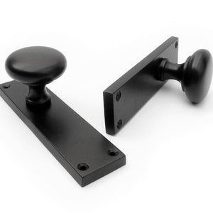 May include: Two matte black door handles. Each handle has a rounded knob and a rectangular backplate with pre-drilled holes for mounting. The hardware is made of metal and is suitable for interior doors. The design is classic.