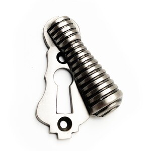 May include: A silver keyhole cover with a decorative, ribbed knob. The knob is attached to the cover and can be turned to open a door or drawer.